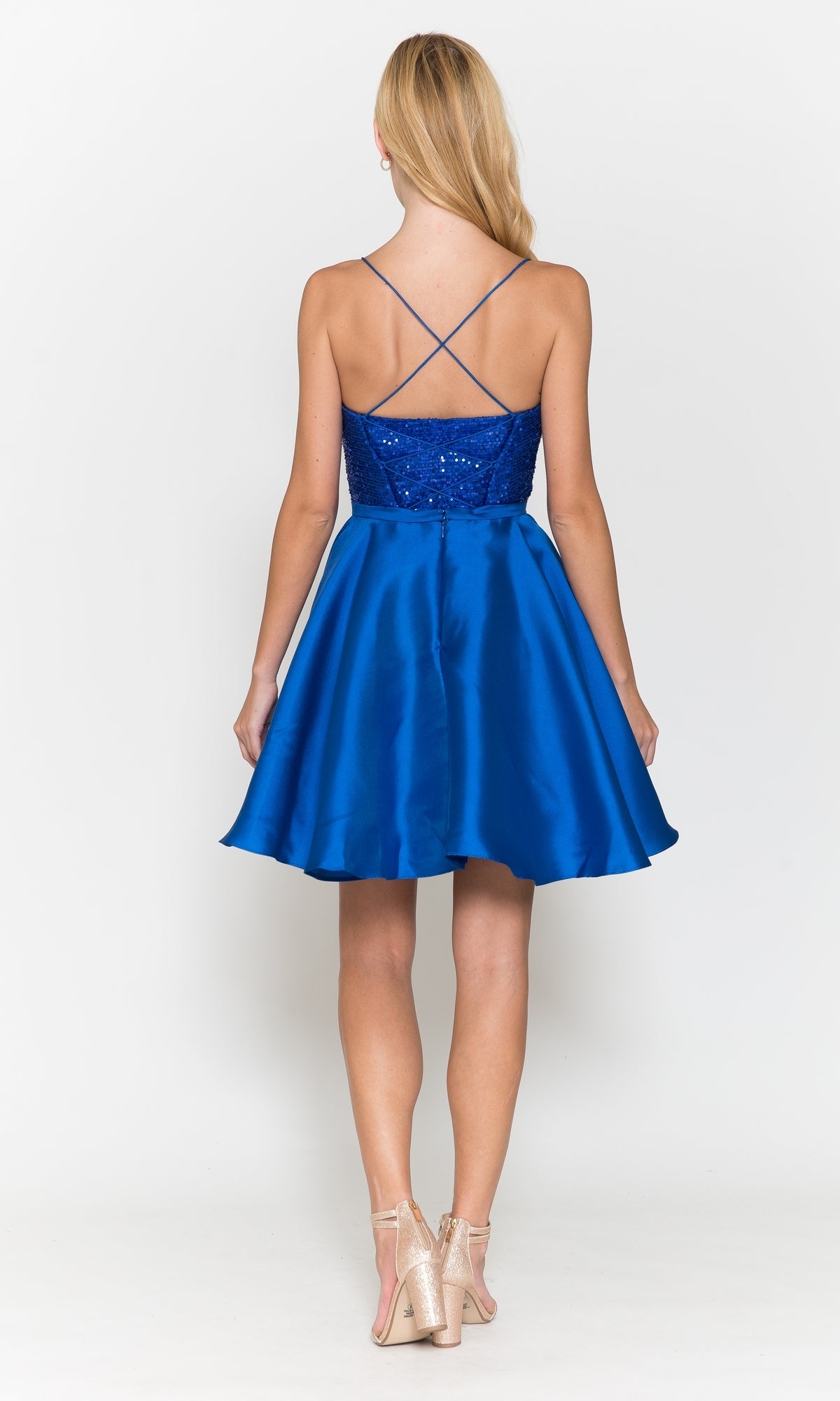 A woman faces away from the camera in the Sequin-Bodice Short Flared Homecoming Dress 8730, a royal blue sleeveless A-line dress with spaghetti straps, paired with nude heels against a plain white background.